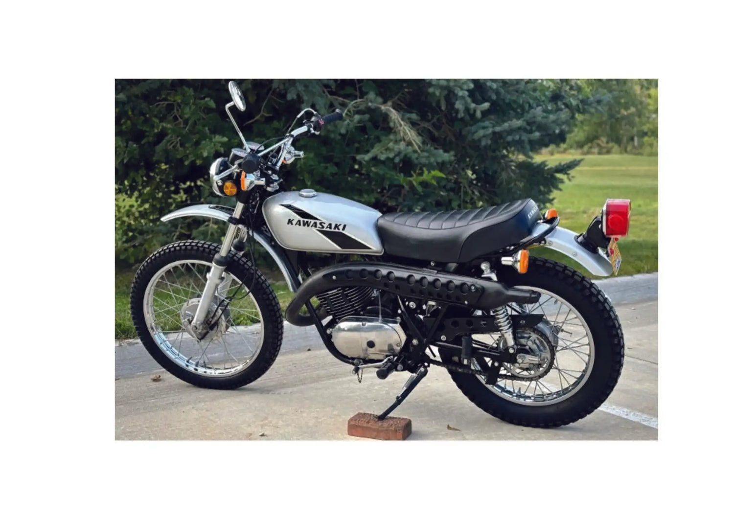 Silver and black kawasaki dirt bike with a matte finish, featuring a classic design and rugged tires.